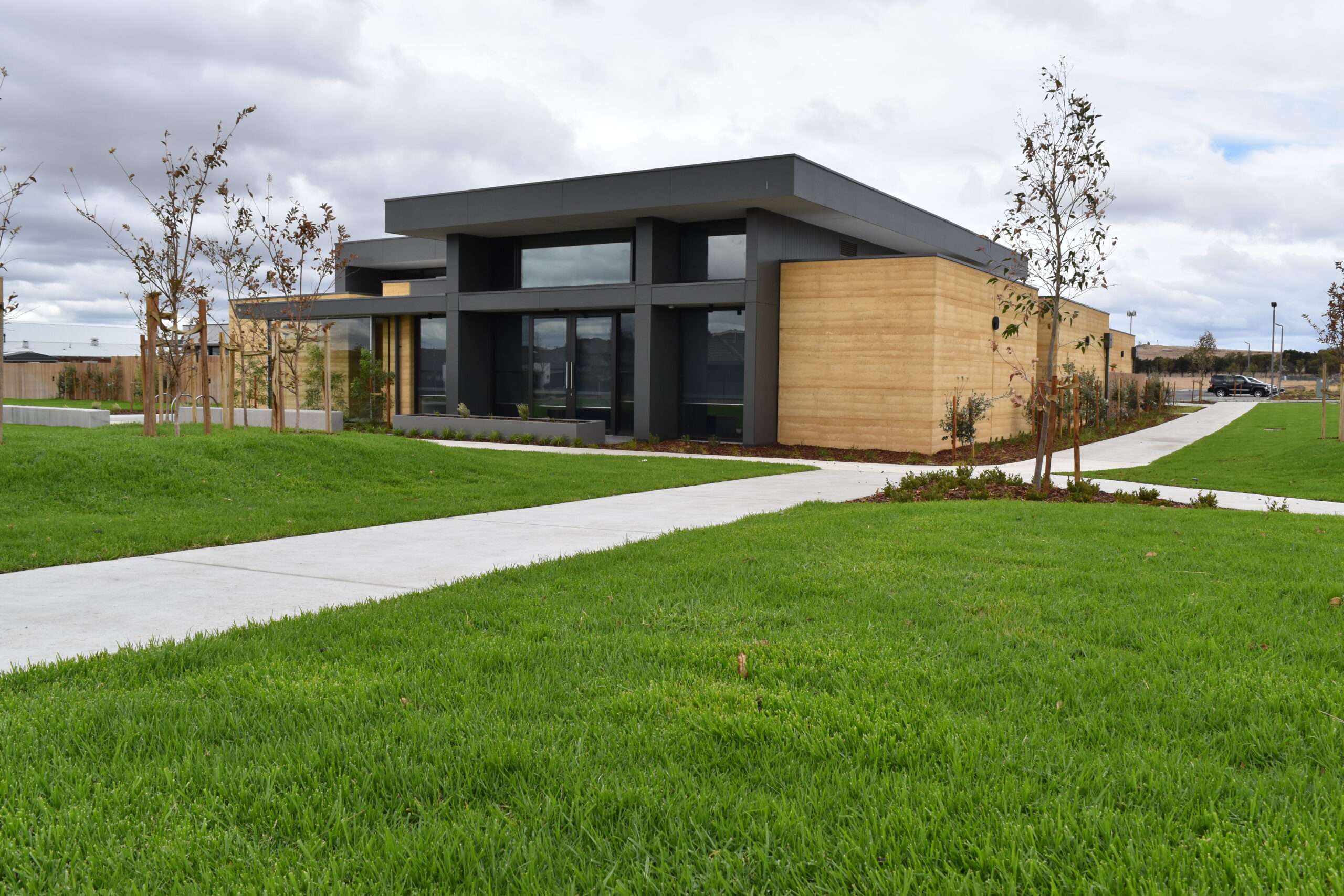 A black and brown modern building with green grass and a tree in front of it