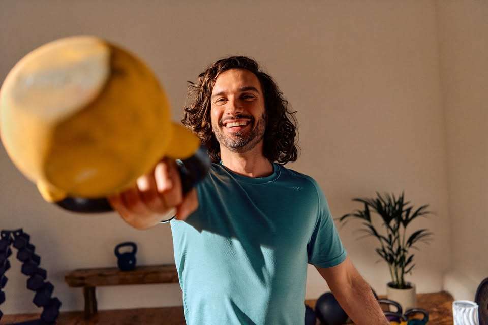 A person wearing a blue shirt holds a yellow kettlebell, showcasing strength in a bright, minimalistic gym setting.