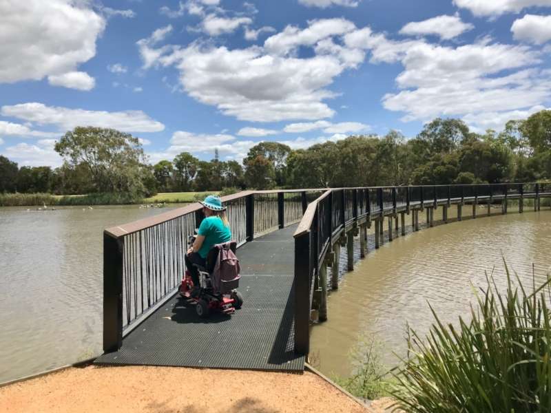 A person in a mobility scooter at the start of Lake Guyatt Footbridge with water