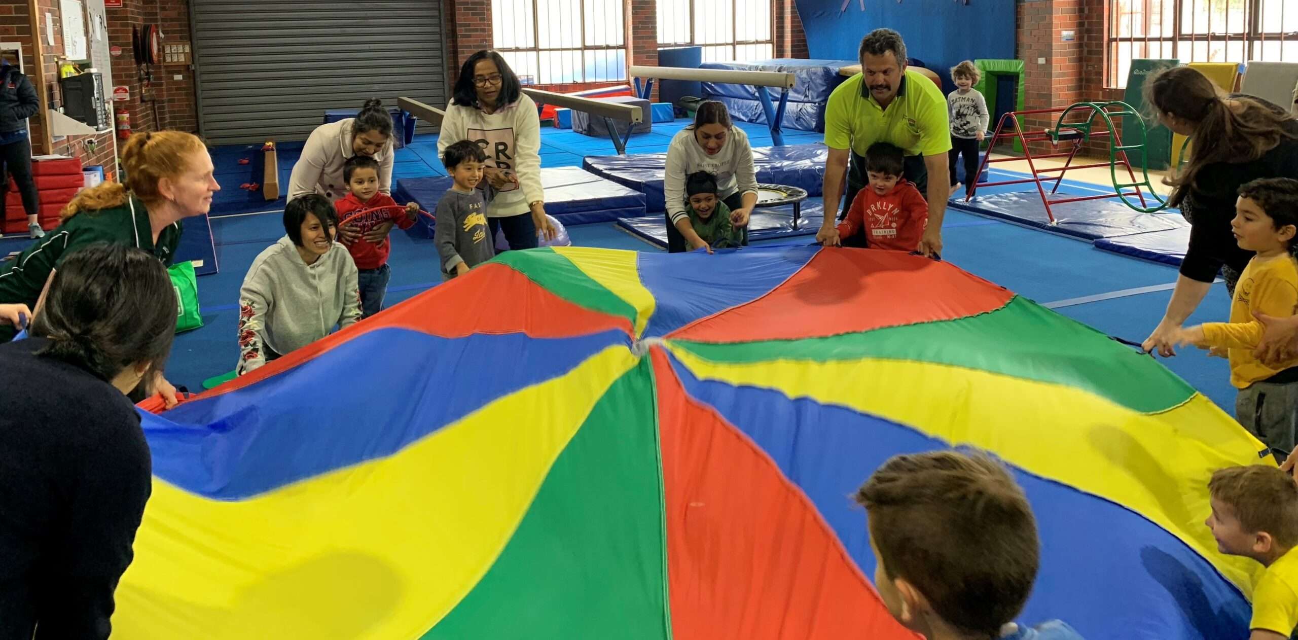 Children and adults play with gymnastics parachute