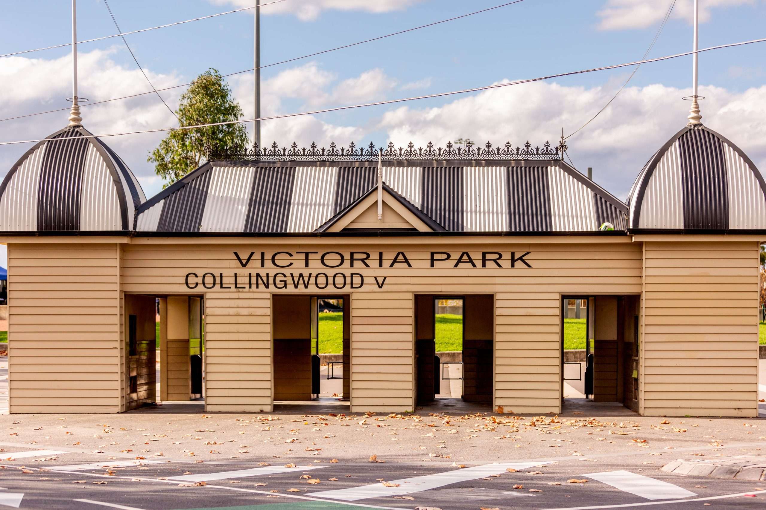 Entrance structure of Victoria Park, Collingwood, featuring decorative domes and a clear blue sky above, surrounded by fallen leaves.