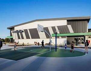 Children playing basketball on a court outside a modern sports center with a sleek design and clear blue sky in the background.