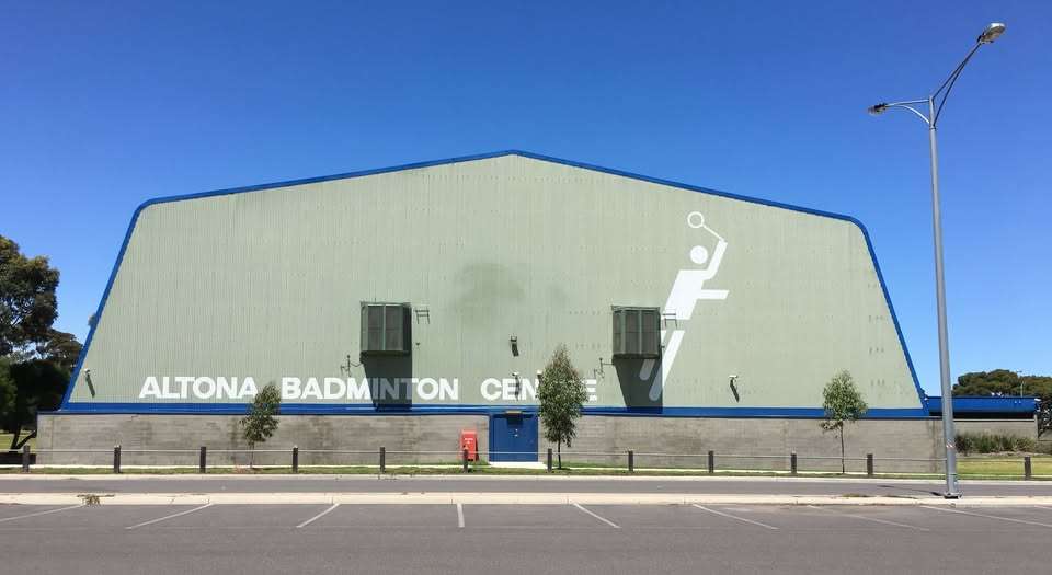 A large green stadium with car parks in front surrounded by trees.