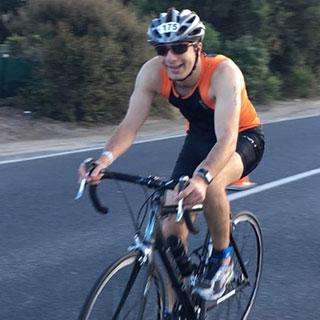 A man riding a road bike in a black and orange suit wearing sunglasses and a helmet
