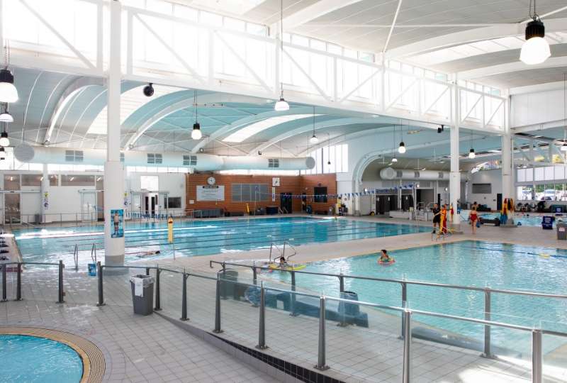 An indoor inground level swimming pool with ramp access to multiple lanes divided by ropes.