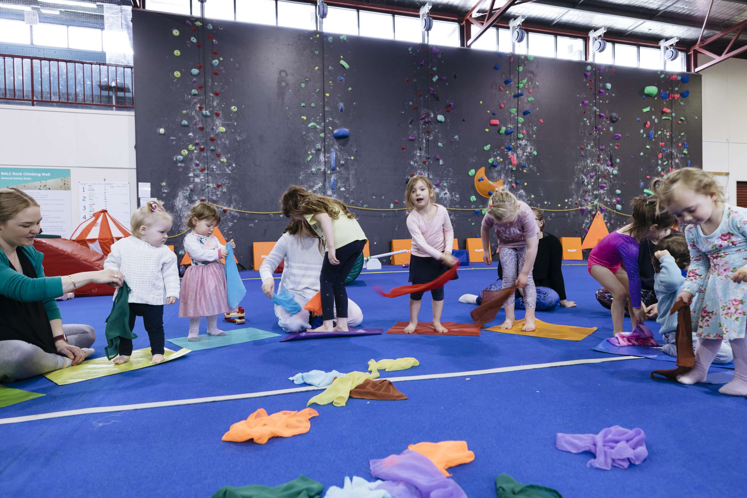 Photo of toddlers in a half circle on a large blue gymnastics mat playing with coloured soft scarves