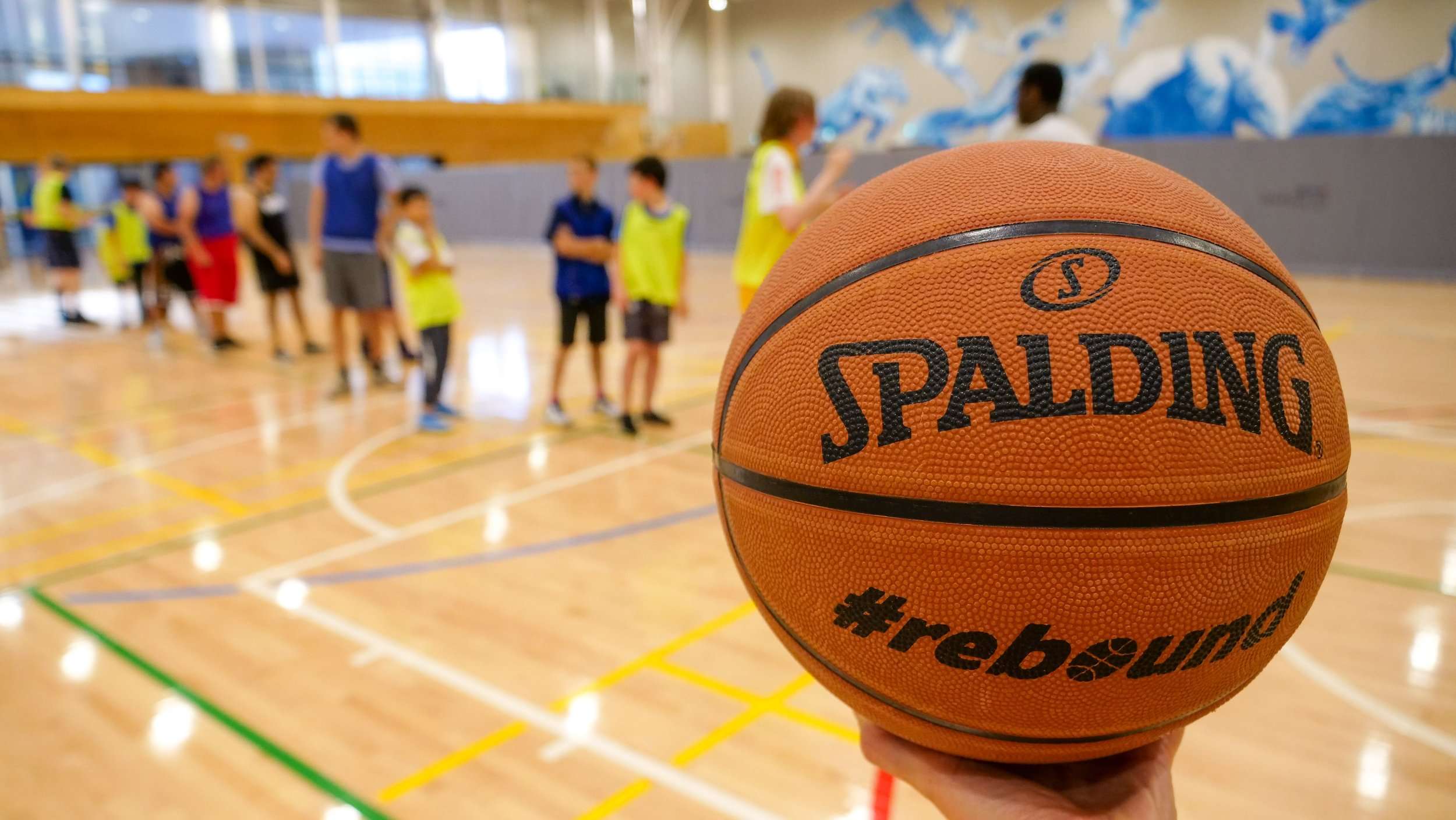 A close-up of a Spalding basketball held in front of children in a gymnasium, participating in a sports activity.