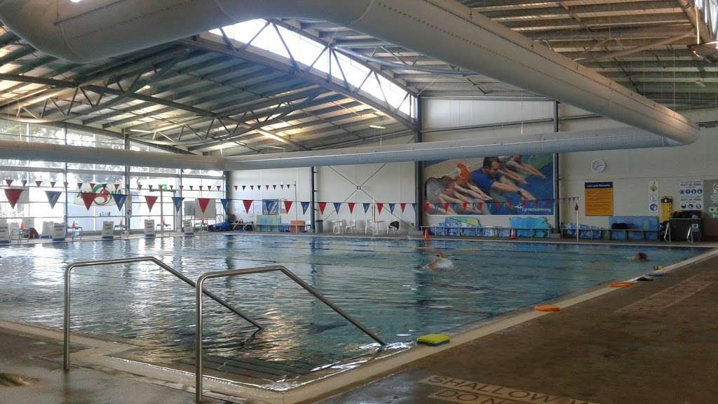 An indoor inground level swimming pool with multiple lanes divided by ropes with multi coloured flags above.