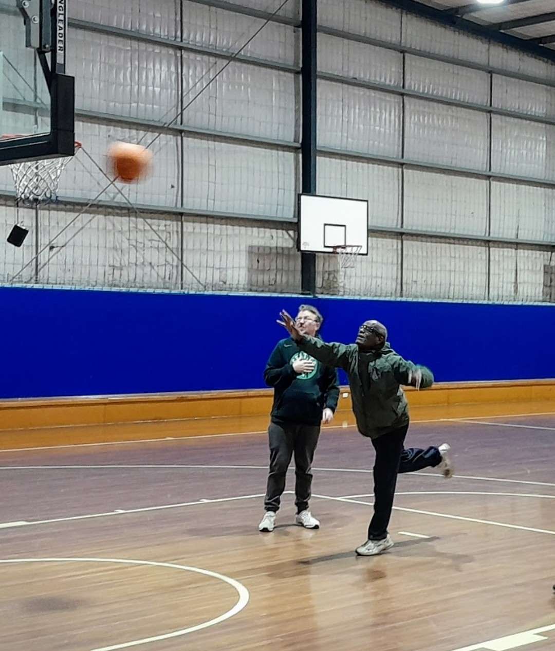 Two individuals practice basketball in a gym, one preparing to shoot while the other holds a ball, focused on the game.