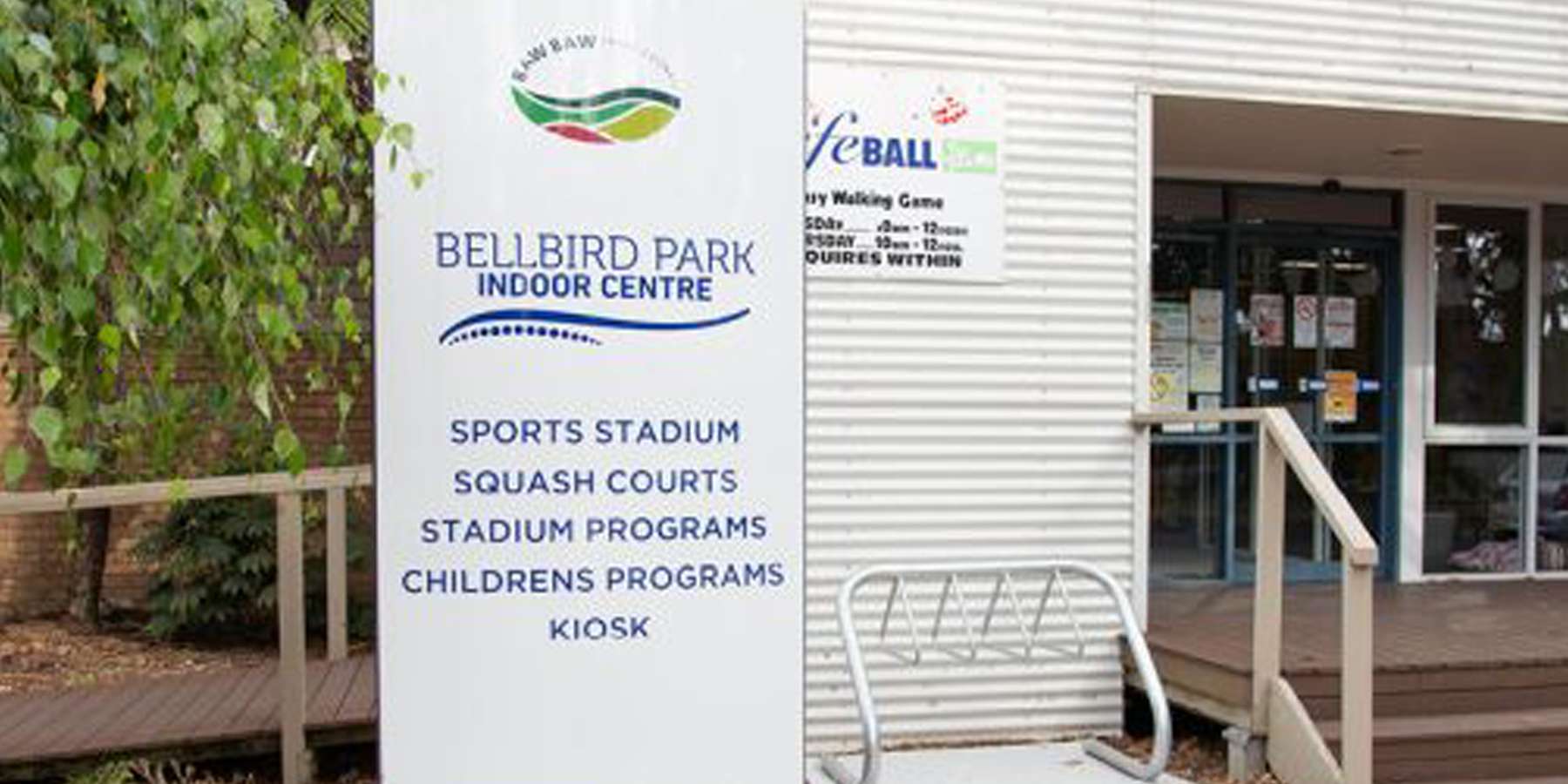 Sign for Bell Street Park Leisure Centre featuring amenities like sports stadium, squash courts, and children's programs, near an entrance.