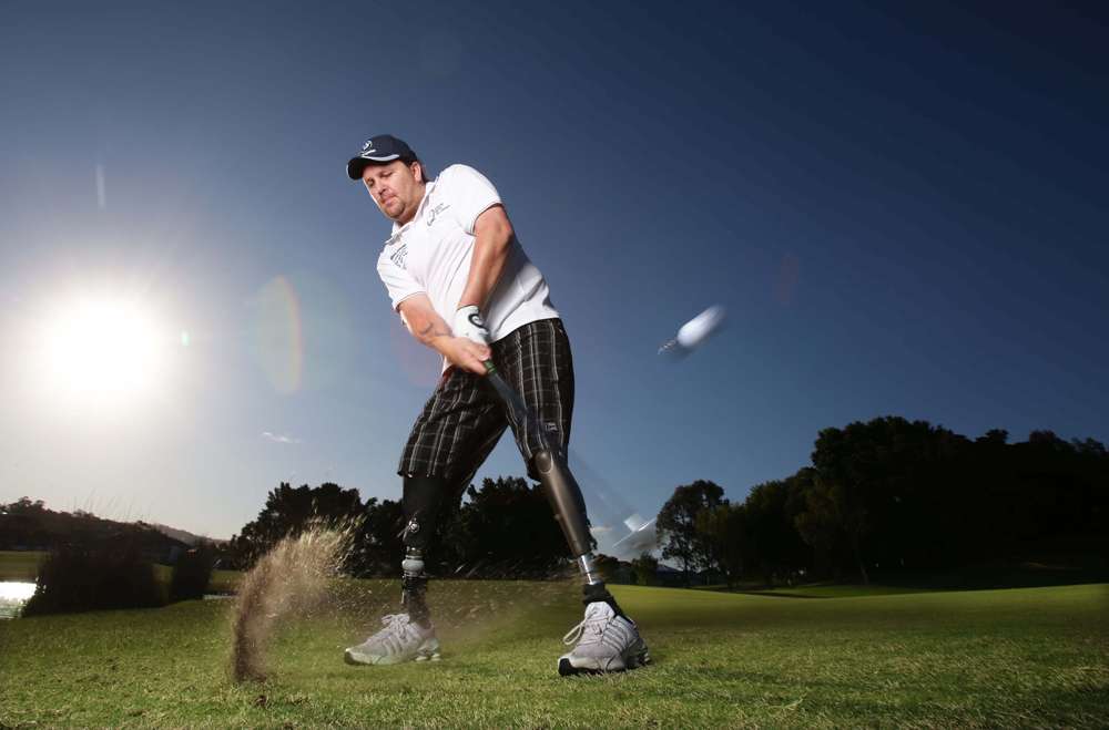 A golfer swings a club on a sunny day, capturing a moment with dust flying from the grass in an outdoor setting.