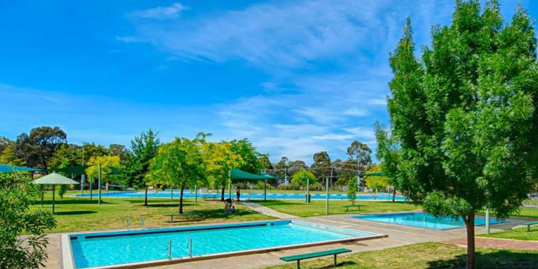 Serene park scene featuring glistening blue pools surrounded by lush greenery and vibrant trees under a bright blue sky.