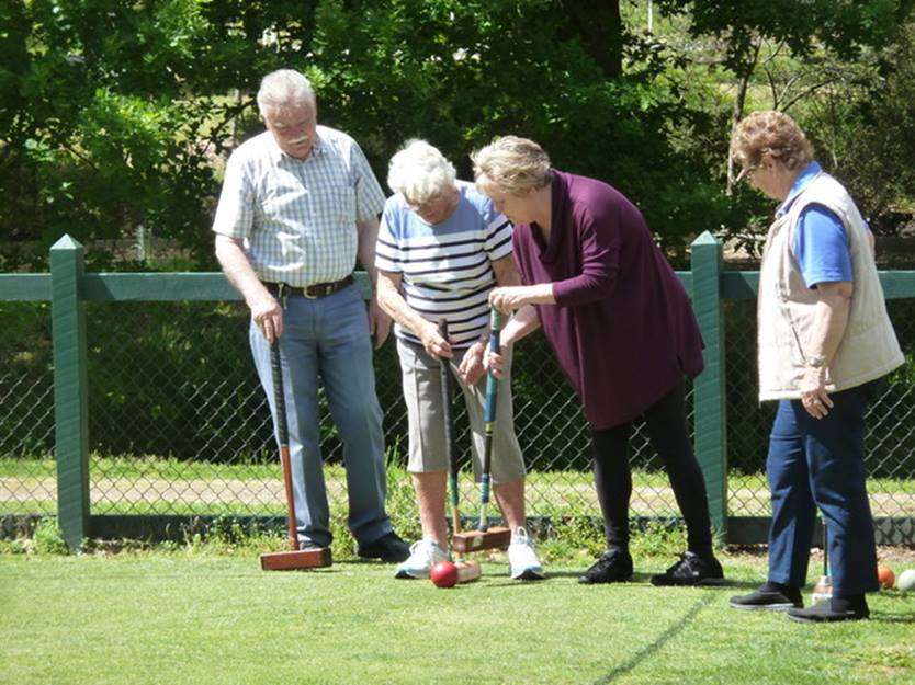 A group of four seniors engage in a croquet game, focusing on a ball as they share tips and strategies on a bright, sunny day.