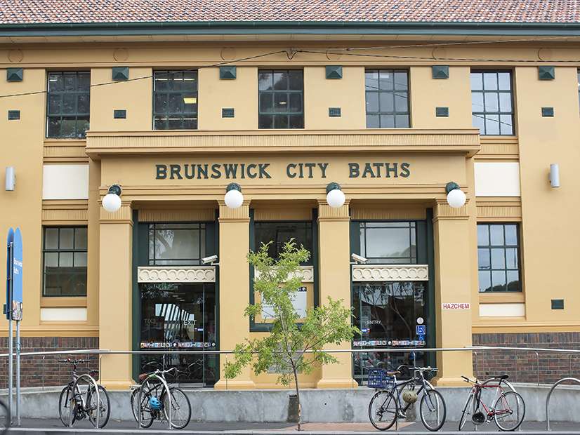 Facade of Brunswick City Baths, featuring yellow walls, large windows, and bicycles parked outside.
