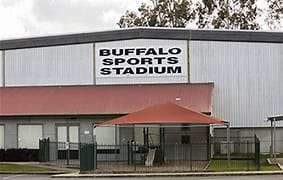 Image displays a sports stadium in Woodend. The building is grey and brown, with a black and white sign that says Buffalo Sports Stadium