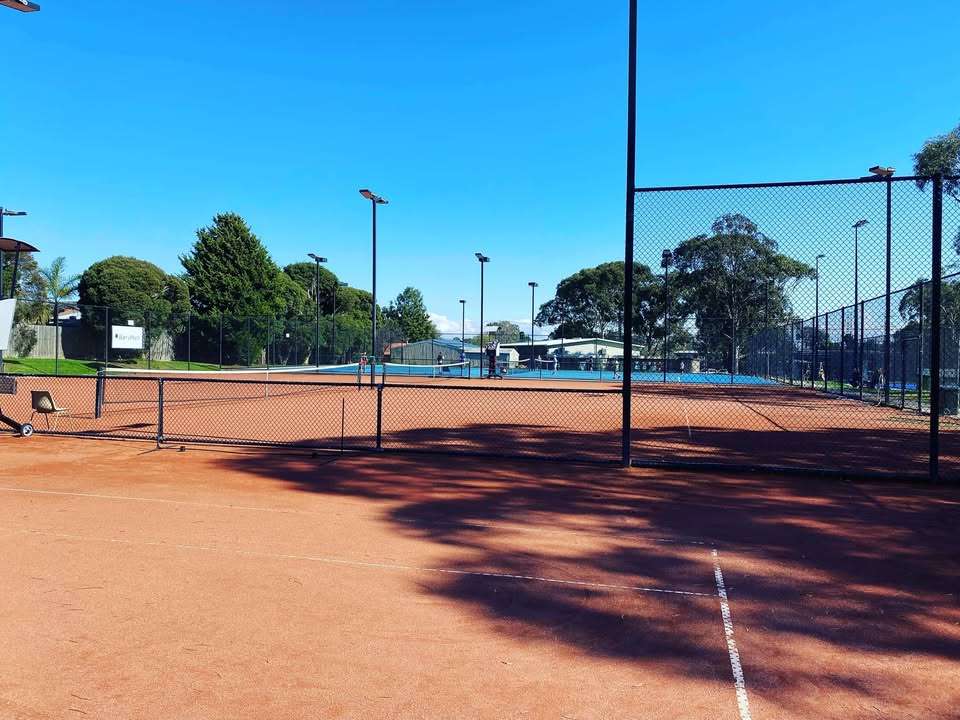 A large tennis court with red colour surface and lights.