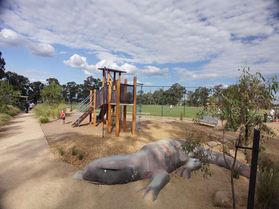 A playground featuring a large lizard structure at the front and an oval in the background