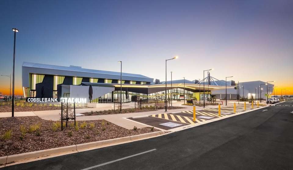 A large white stadium surrounded by concrete, roads and plants.