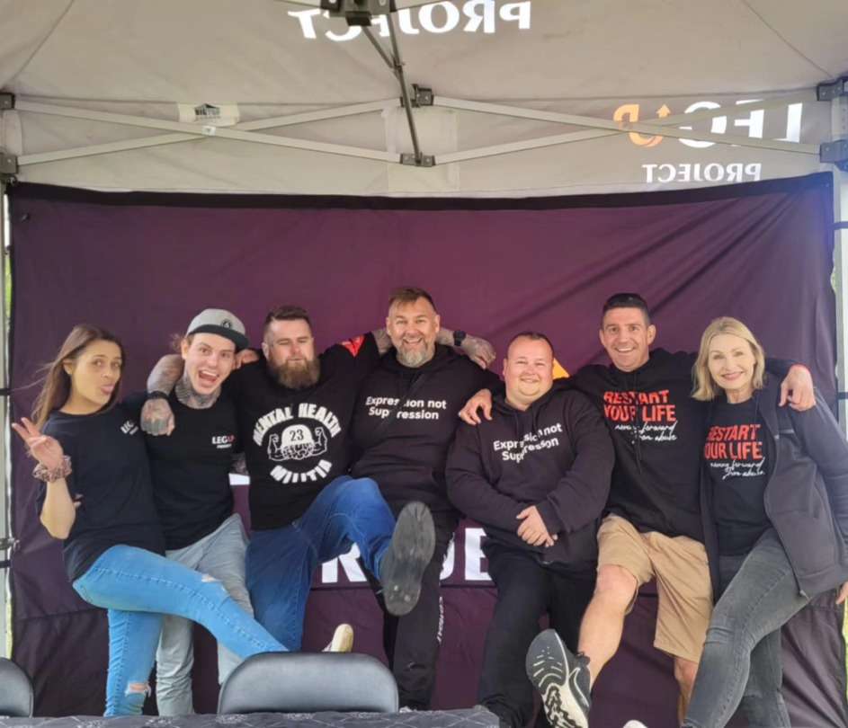 A Group of people arm in arm kicking their legs up and smiling.