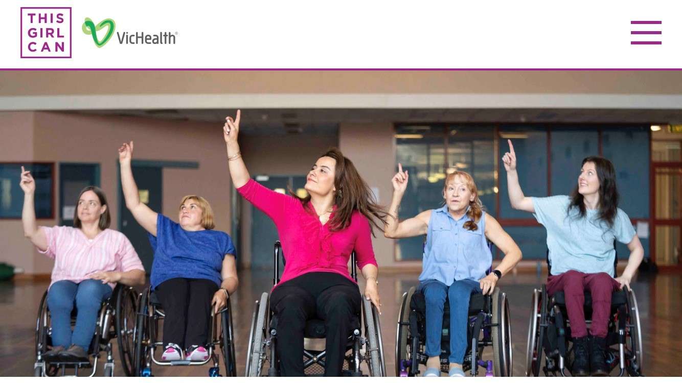 Five women in wheelchairs enthusiastically raise their arms, celebrating empowerment and inclusion in a supportive atmosphere.