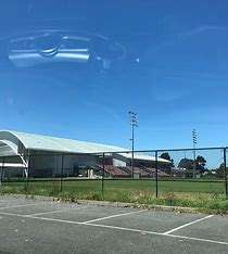 Image displays the Darebin Sports centre, the building is in the background, there is a green field behind a black wire fence, and a carpark