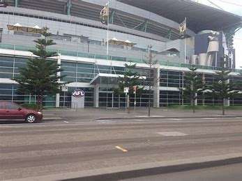 Exterior view of an AFL building with glass windows and tall trees along the sidewalk, featuring a purple AFL logo.