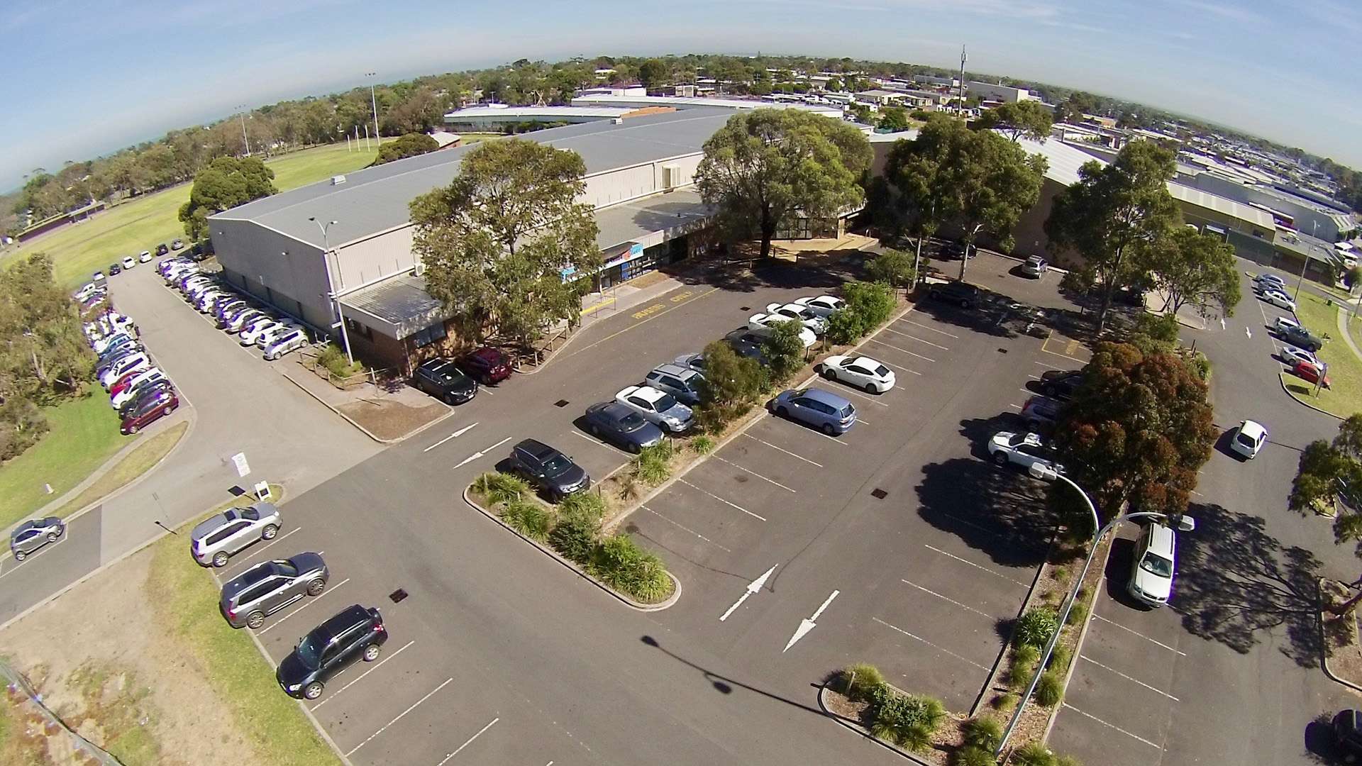 A large grey stadium surrounded by car parks and trees.