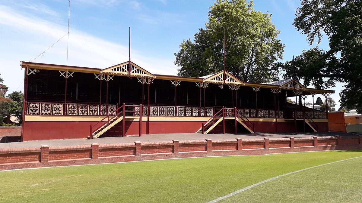 A large red and cream timber grandstand surrounded an oval of green grass.