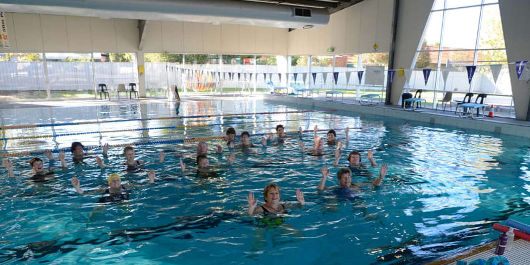Aqua fitness class in a bright indoor pool, featuring participants immersed in water, focusing on exercise and movement.