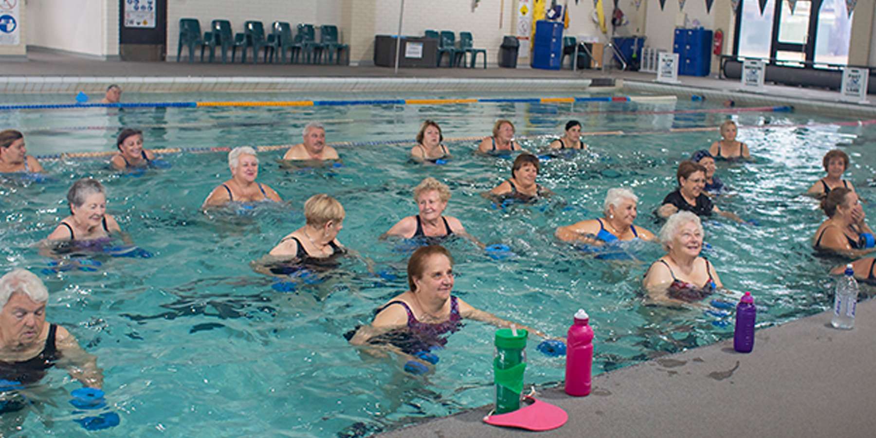 A group of seniors participates in a water aerobics class in a pool, surrounded by colorful water bottles and a supportive atmosphere.