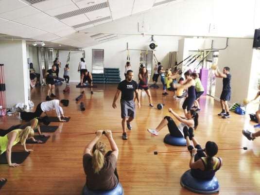 A bustling fitness class with diverse participants engaged in various exercises using mats, weights, and balance balls in a bright studio.