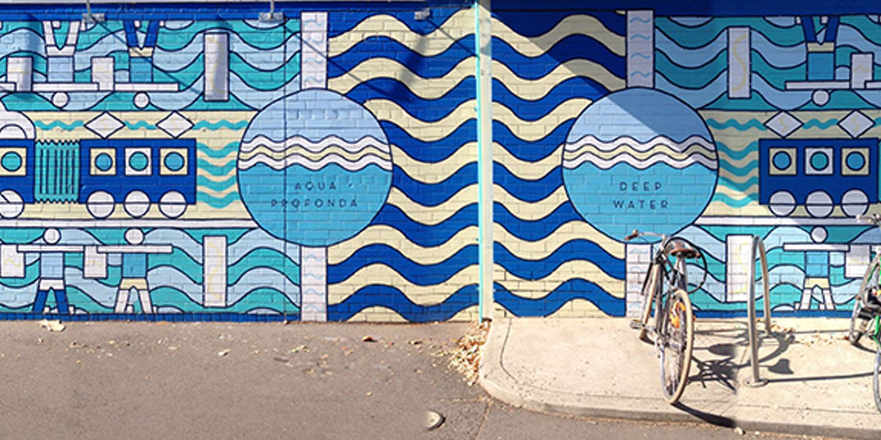 Vibrant blue mural featuring wavy patterns and circular designs, set against a street scene with a parked bicycle.