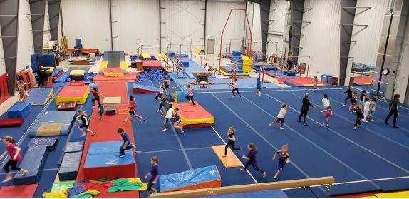 A bustling gymnastics facility with children practicing on colorful mats and equipment in a spacious, bright indoor environment.