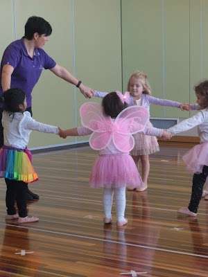 a group of young children in a circle holding hands with their teacher.