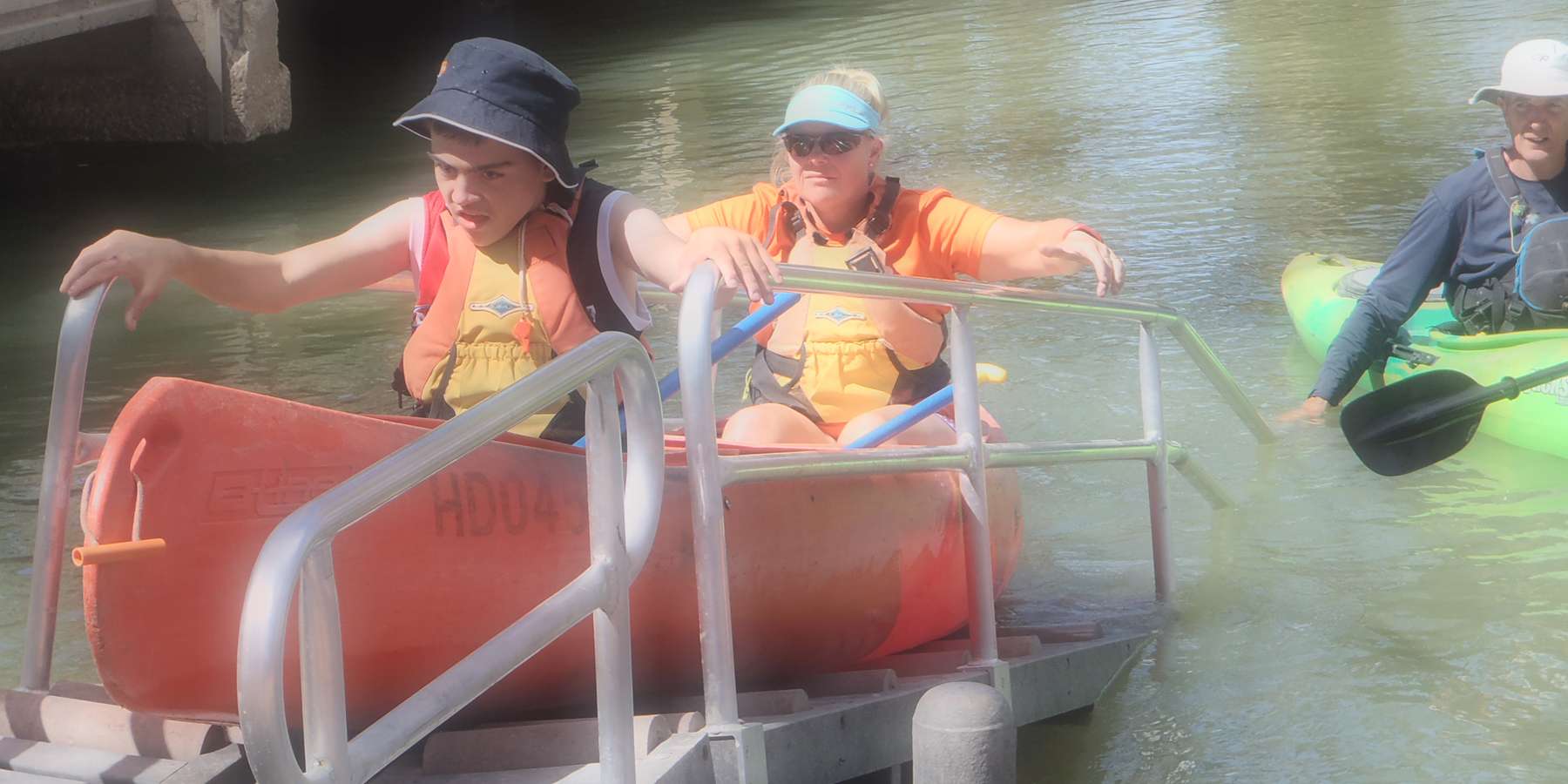Image of an accessible Canoe Launcher at Kings Billabong Park, there are two people in a red canoe wearing hats and life jackets ready to be launched