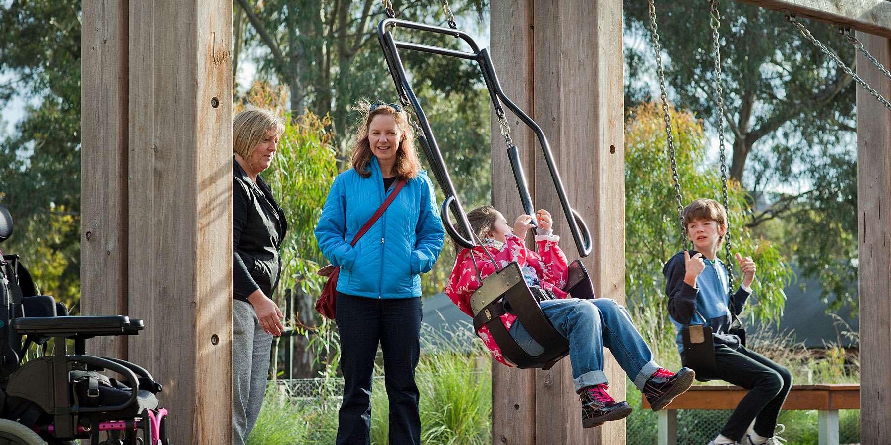 Children playing on all abilties swing set in a playscape