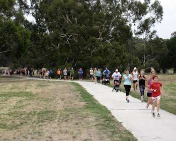 Green space with trees in the background and people running on a footpath
