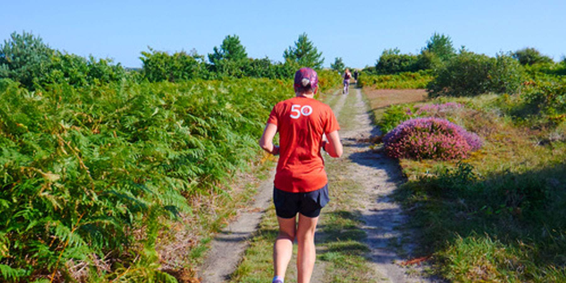 Image taken from behind a runner, running on a dirt road in a green open space