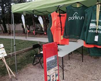 Image of the parkrun finish line in the background with a marquee and parkrun merchandise in the foreground