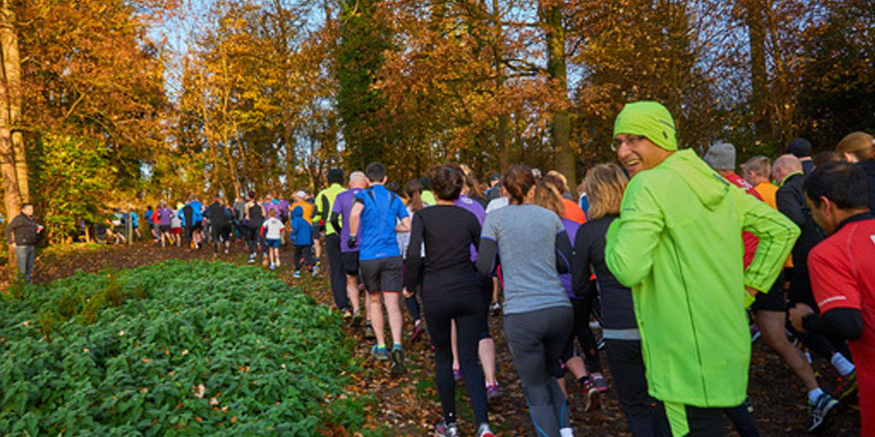 Image taken at the back of a group of people running. One man has turned his head and is looking at the camera smiling