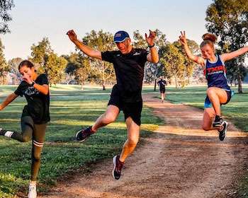 Image of three people jumping in the air with a green space and footpath in the background