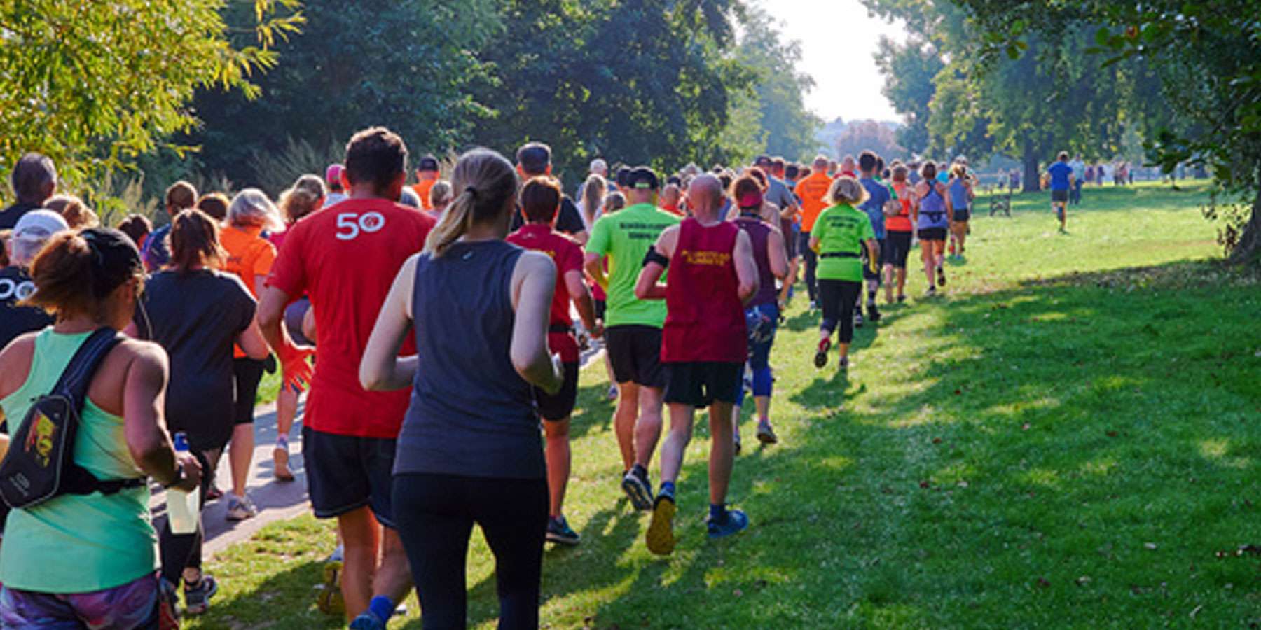 Image taken from behind a group of people running on a footpath in a green space