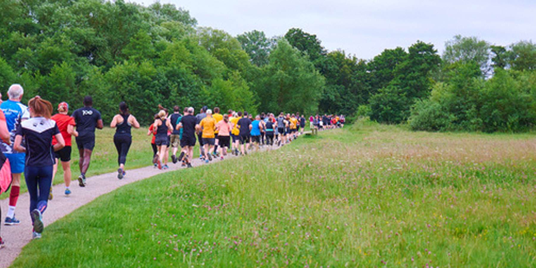 Image taken from behind a group of people running on a footpath in an open space with trees in the background