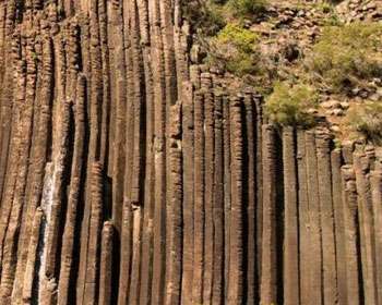 Vertical basalt columns rise from rocky terrain, showcasing natural geological formations and sparse vegetation on the hillside.