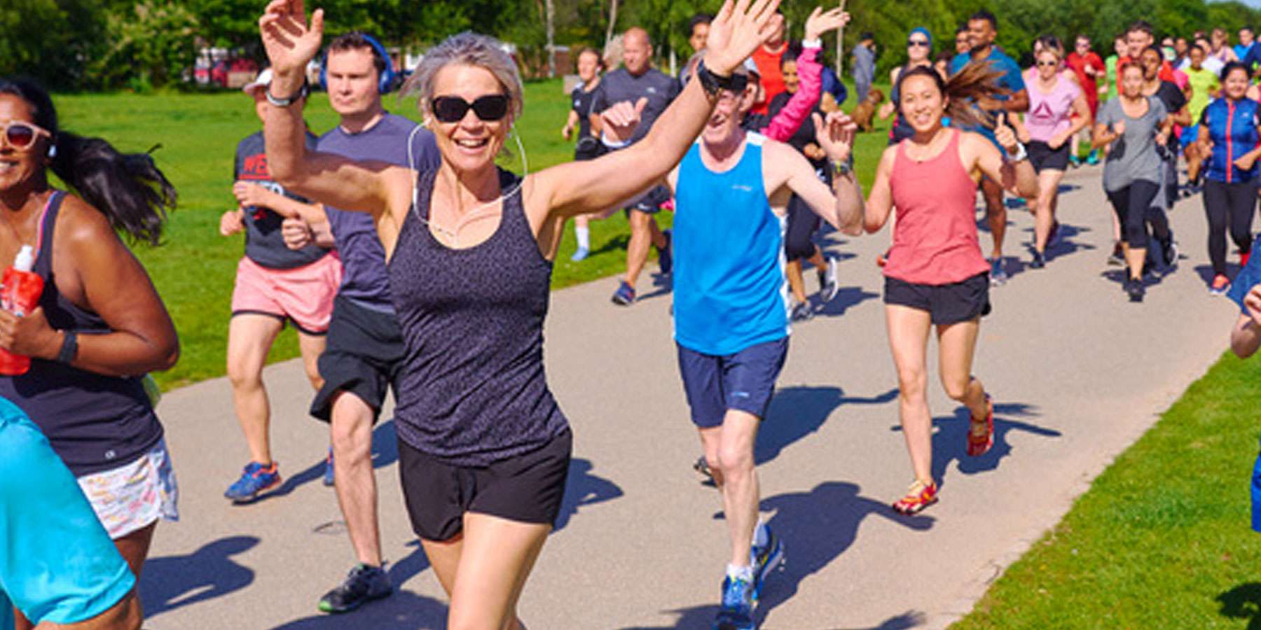 Image of people running on a footpath. The woman at the front of the group is smiling with her hands in the air