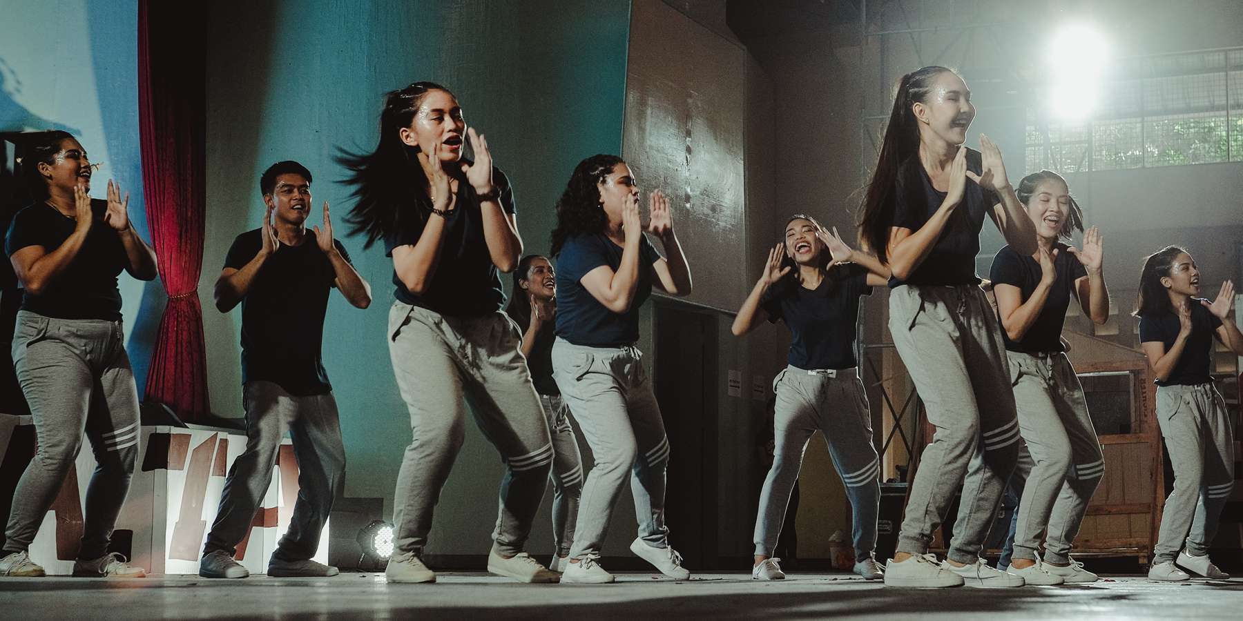 Image of a group of dancers, all wearing great pants and black t-shirts, dancing.
