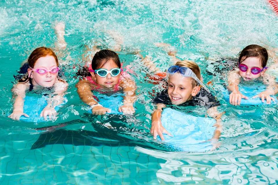 4 children swimming with kick boards in the pool.