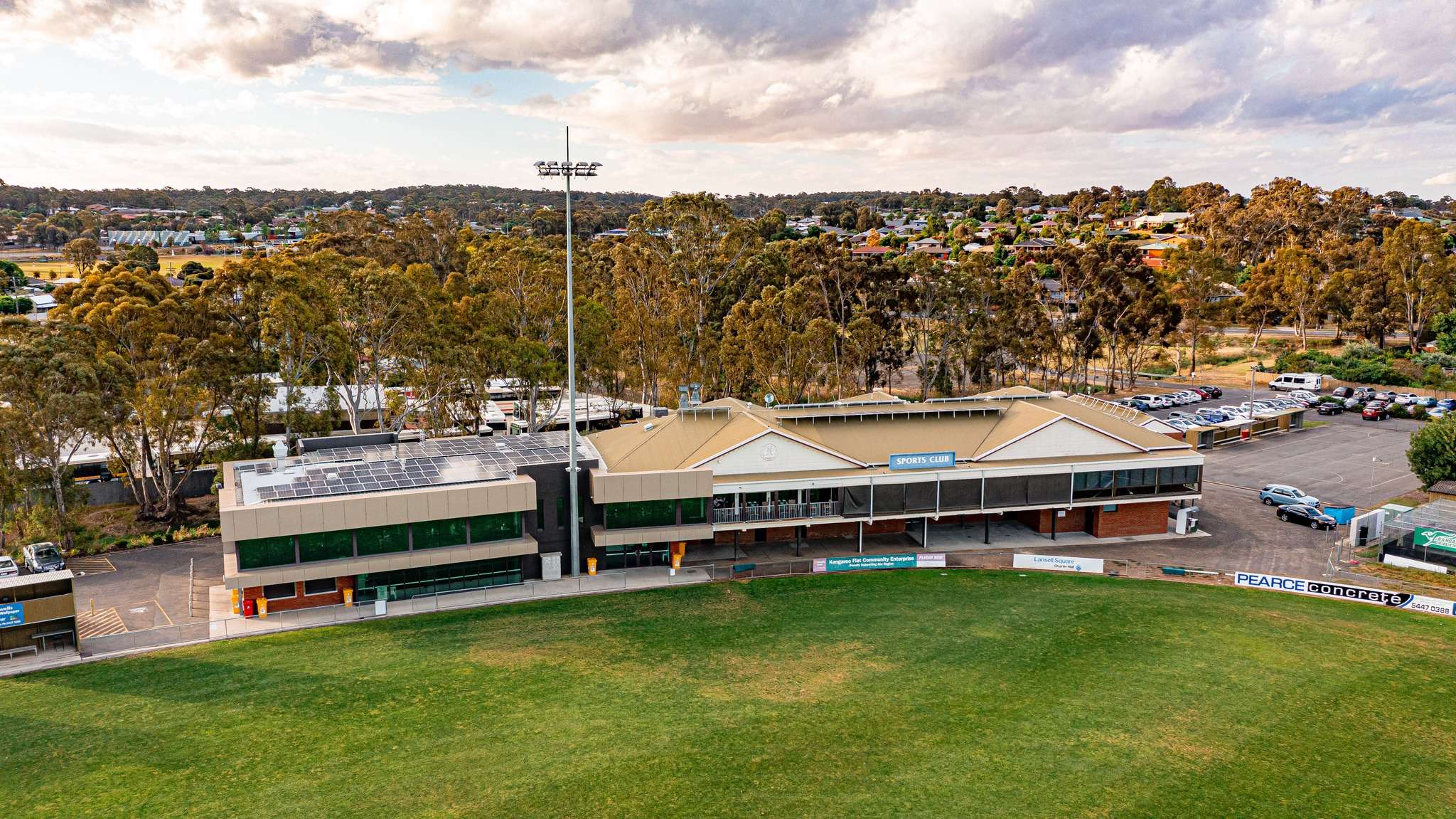 A large green oval surrounded by a large grand stand and many trees in the background.