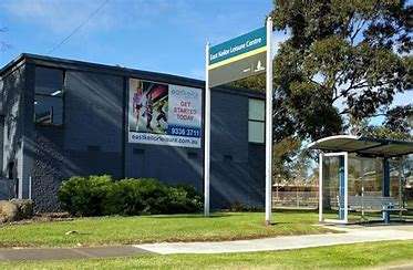 Exterior view of the East Kildare Leisure Centre, featuring a sign and a bus stop in front, with green grass and trees nearby.