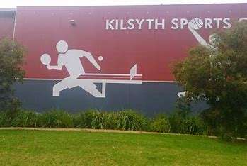 A mural of stick figure athletes running and playing sports on the wall of Kilsyth Sports, surrounded by greenery.